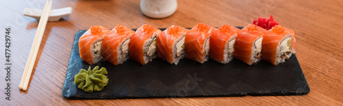 black plate with tasty sushi rolls near chopsticks on wooden table, banner