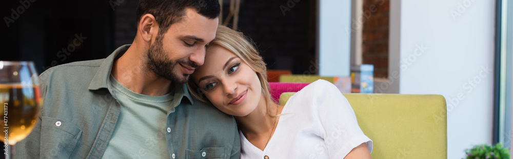 happy woman leaning on shoulder of boyfriend near blurred glass of white wine, banner happy woman leaning on shoulder of boyfriend near blurred glass of white wine, banner