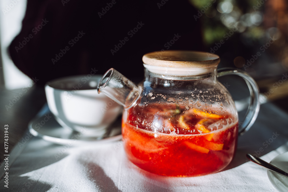 Unrecognizable woman sit in cafe with glass pot of hot winter tea by table with white tablecloth. Unrecognizable woman sit in cafe with glass pot of hot winter tea by table with white tablecloth.