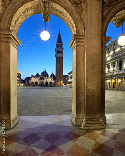 Doge Palace in Venice, Campanile tower and basilica on Piazza di San Marco visible through ancient arch with circle street lamp. Romantic evening, night in Venice, Italy. Center of town at dawn. © tilialucida