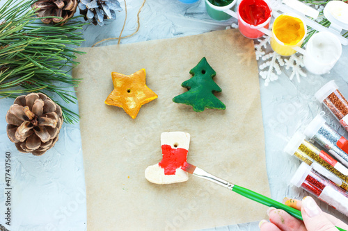 Fototapeta Naklejka Na Ścianę i Meble -  a brush with red paint paints a Christmas sock, DIY toys for the New Year, creative decoration for a Christmas tree made of salt dough