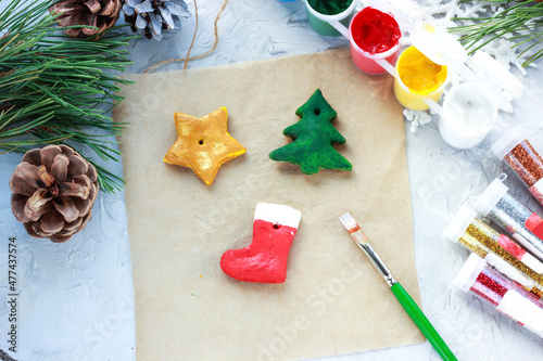 Fototapeta Naklejka Na Ścianę i Meble -  a brush with red paint paints a Christmas sock, DIY toys for the New Year, creative decoration for a Christmas tree made of salt dough