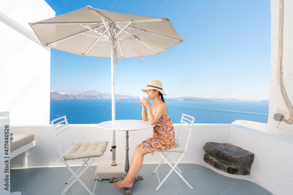 An Asian woman enjoy drinking coffee while sitting on the outdoor terrace of the island, Santorini, Greece