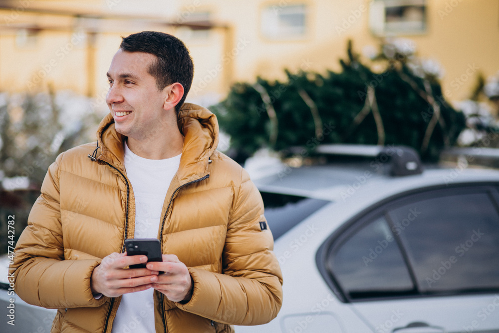 Handsome man talking on phone by the car with christmas tree on top