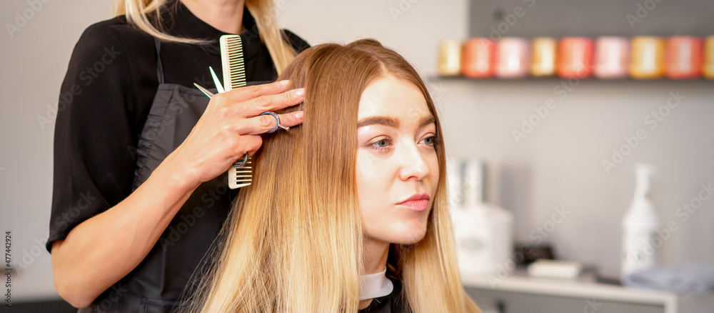 Fototapeta premium Gorgeous blonde long hair woman and her hairdresser looking and checking out hairstyle. Beautiful hairstyle of a young blonde woman after dying hair in a beauty salon, results of hair treatment