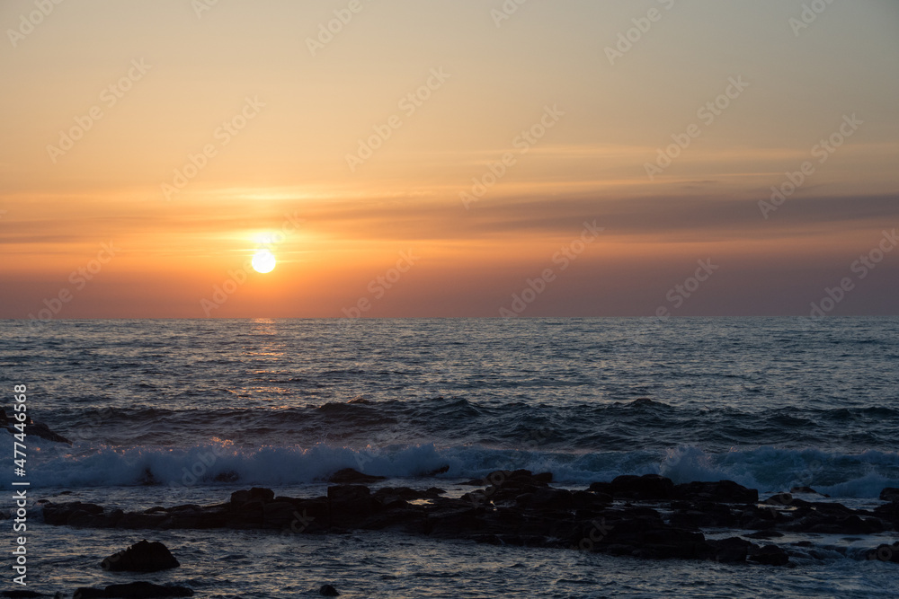 水平線に沈む夕陽と岩の海岸
