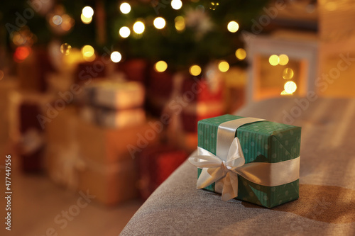 Christmas gift box on sofa against blurred lights indoors. Space for text