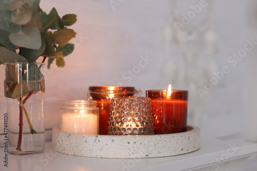 Burning candles on mantel near white wall indoors photo