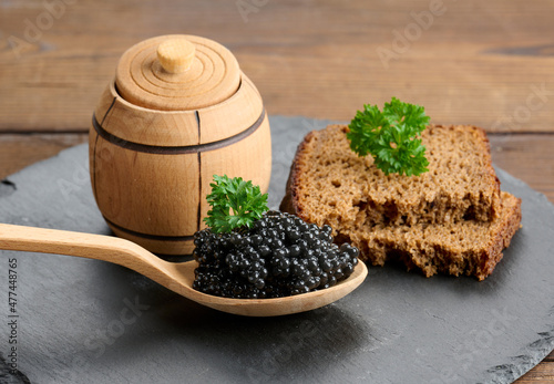 fresh grainy black paddlefish caviar in brown wooden spoon on a brown table, close up