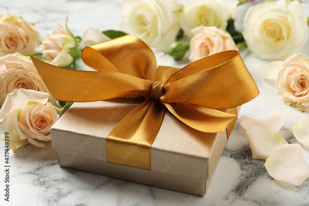 Golden gift box and beautiful roses on white marble table Golden gift box and beautiful roses on white marble table