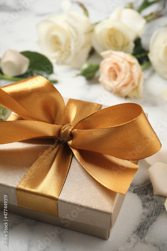 Golden gift box and beautiful roses on white marble table, closeup