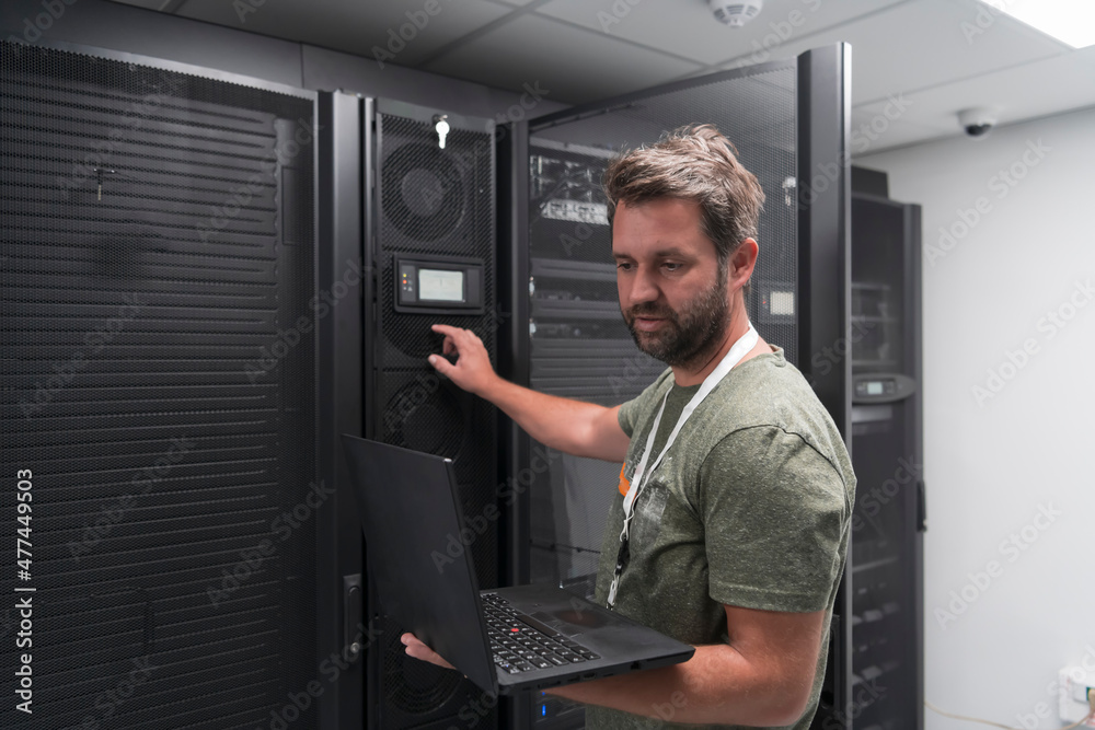 Data Center Engineer Using Laptop Computer Server Room Specialist Facility with Male System Administrator Working with Data Protection Network for Cyber Security or Cryptocurrency Mining Farm. 