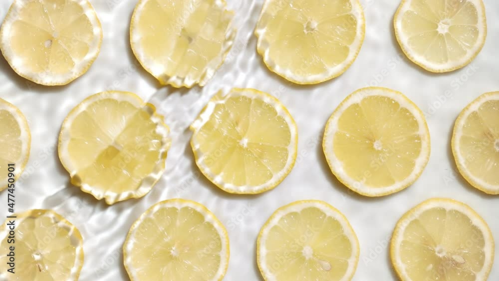 Waves and splashes on water surface over lemon slices arranged in lines on white background | skincare background, face wash commercial