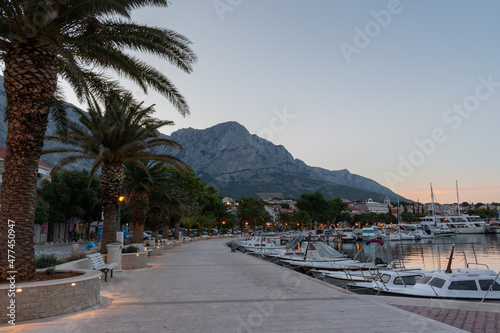 Empty promenade and moored boats in marina in touristic resort Baska Voda, Croatia at dawn in summer