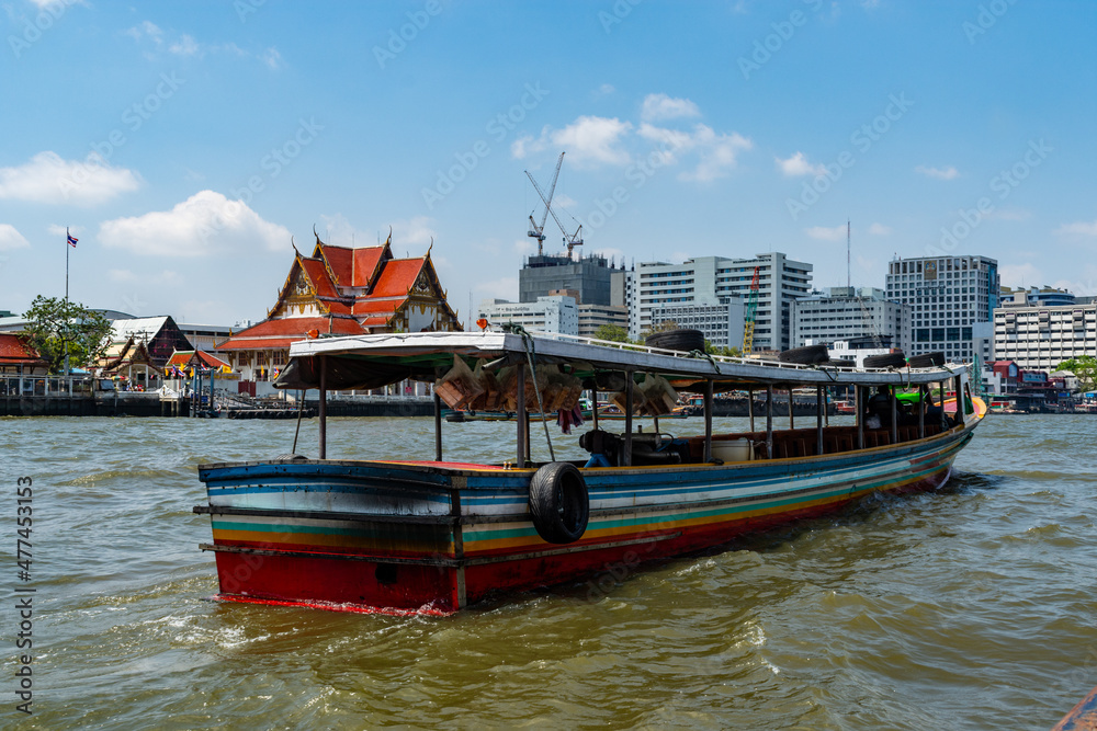A long boat on Chao Phraya River with Wat Rakhangkhositaram in the background, Bangkok, Thailand.
