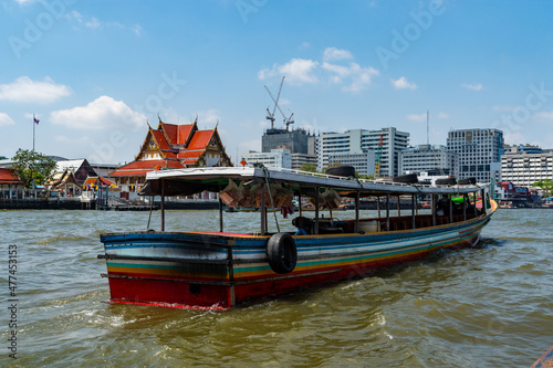 A long boat on Chao Phraya River with Wat Rakhangkhositaram in the background, Bangkok, Thailand.