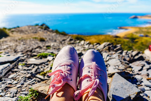 Female legs in sneakers against coast landscape, Spain.