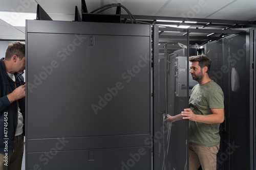  Technicians team updating hardware inspecting system performance in super computer server room or cryptocurrency mining farm.