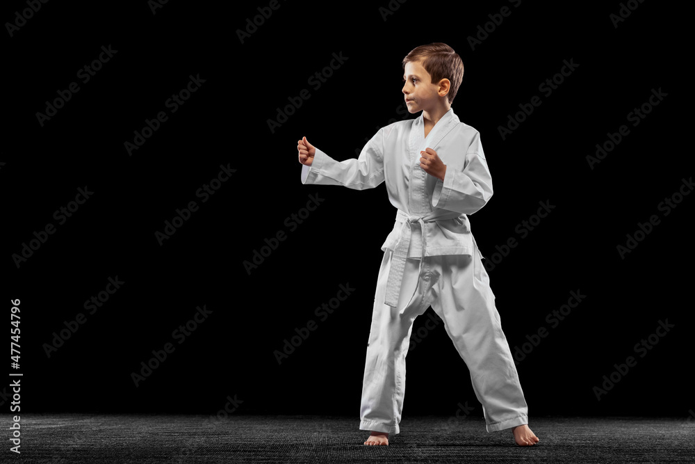 One little kid, boy, taekwondo athlete posing isolated over dark background. Concept of sport, education, skills