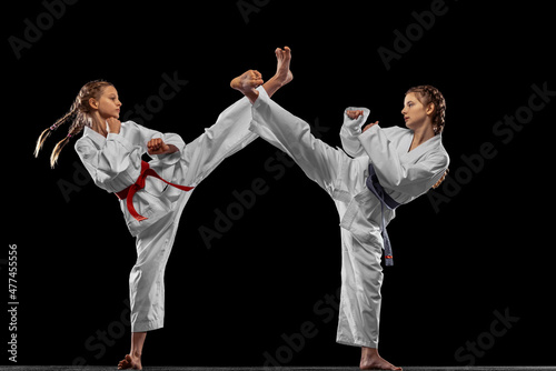 Two young girls, teens, taekwondo athletes training together isolated over dark background. Concept of sport, education, skills