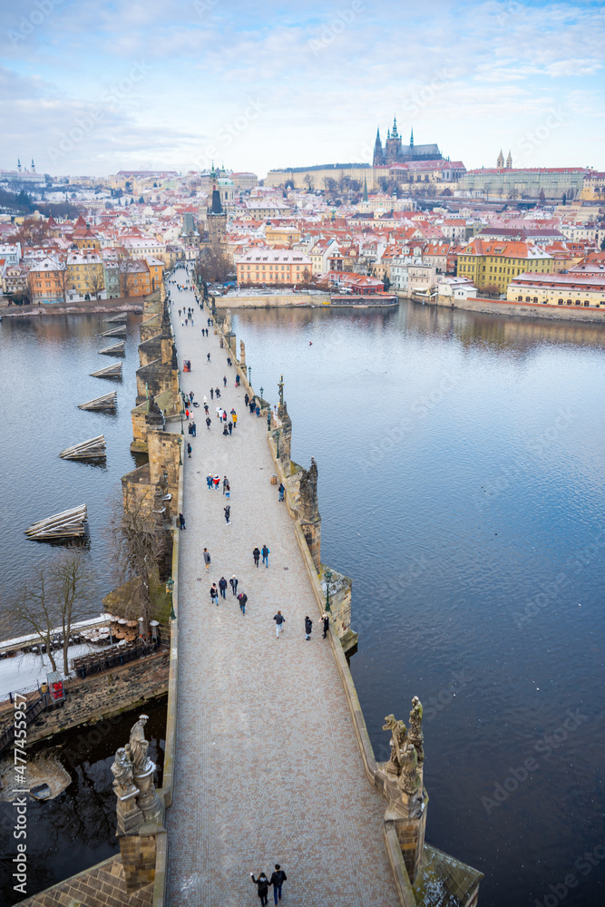 Naklejka premium People are walking on Charles bridge, whose rooftops are covered by snow, Prague in the winter