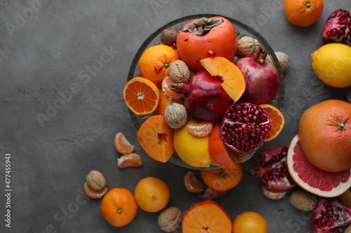 Many different seasonal fruits and walnuts in a plate on a beige table. Background with nuts  tangerines  pomegranates  grapefruits  persimmons and lemons
