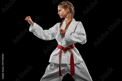 One young girl, teen, taekwondo athlete posing isolated over dark background. Concept of sport, education, skills