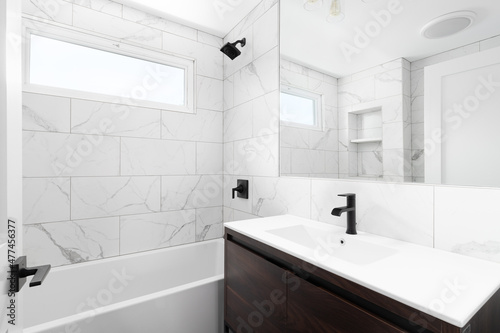 A renovated bathroom with a wood vanity cabinet  white marble sink and large marble tiles lining the shower walls.