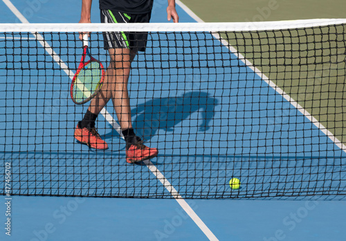 Tennis player with racket and ball on blue hard tennis court near net. Sports, active game background, tennis tournament, match concept. photo