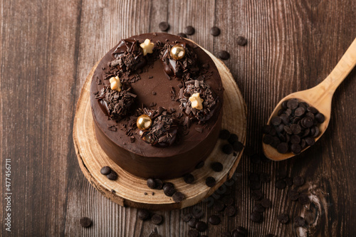 Overhead view of chocolate cake, with chocolate chips, spoon and wooden table.