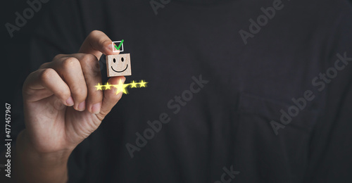 Customer service evaluation and satisfaction survey concepts. Customer hand picked the happy face smile face icon give five star excellent on wooden cube on wooden cube on table.