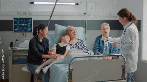 Little girl and mother visiting grandpa in hospital ward while doctor consults him for recovery. Medic explaining diagnosis to ill patient and family in visit at clinic. Physician at checkup