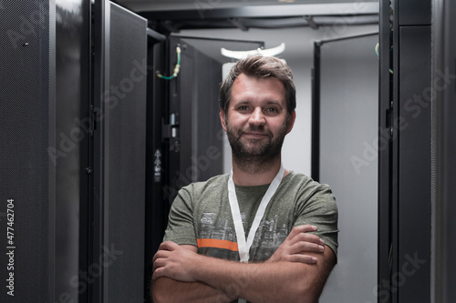 Portrait of male technician or network administrator standing brave as a hero with arms crossed in data center server room.