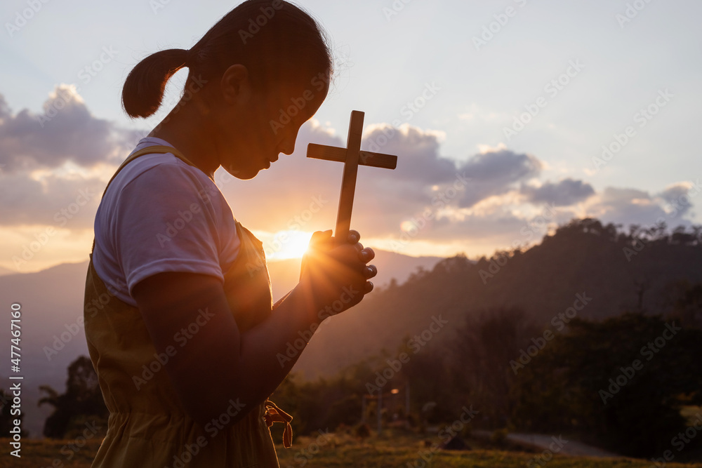 Silhouette of young girl praying to the GOD while holding a crucifix
