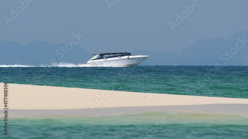 Empty bar of fine sand at island in tropical sea, speedboat rush across water on back, seen blurred in heat-haze. Selective focus on sand bar at foreground photo