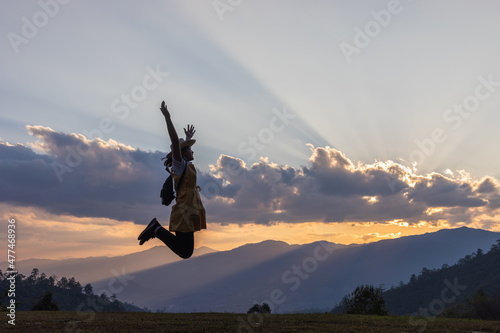Silhouette happy beautiful girl with backpack and hat jumping on mountain park over sunset background.