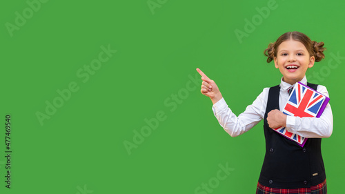 A schoolgirl with an English textbook smiling points her finger at the advertising. a little joyful girl on a green isolated background. obtaining knowledge and education in primary school.