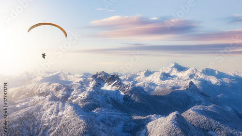 Adventure Composite Image of Paraglider Flying up high in the Rocky Mountains. Sunny Sunset Sky. Aerial Background from British Columbia, Canada. Extreme Sport Concept. Panorama. winter