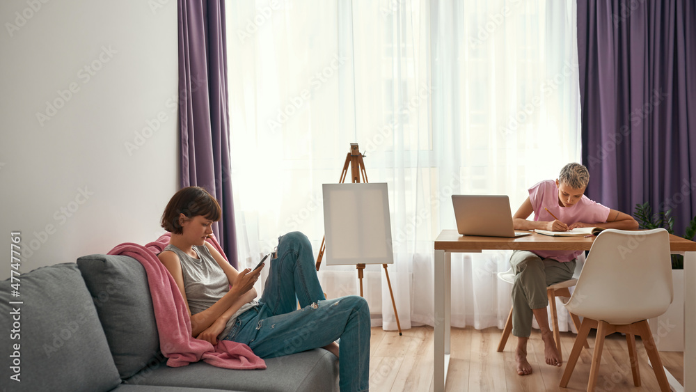 Girl watch on phone while girlfriend do homework