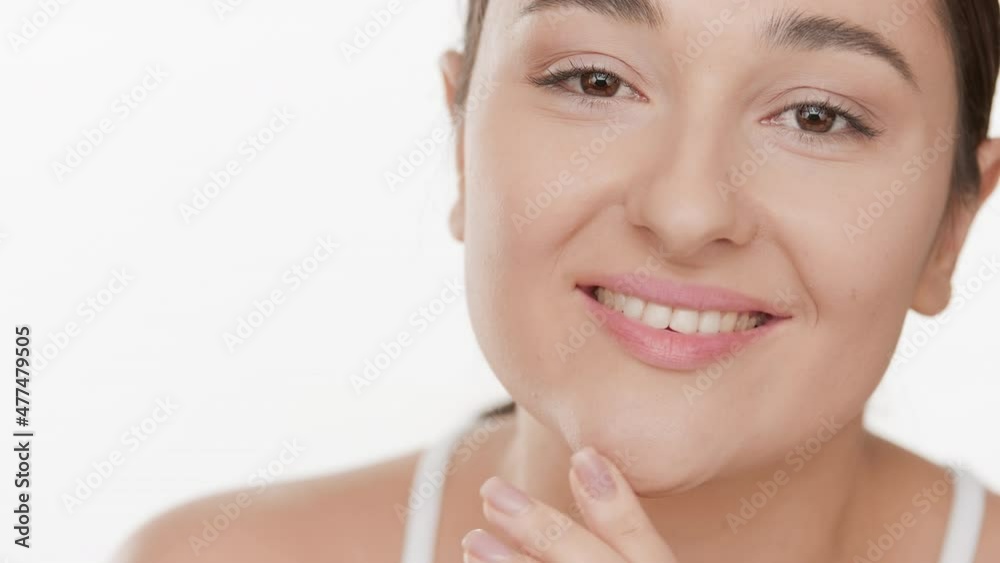 Close up beauty portrait of young cute Caucasian brown-haired woman in white bra strokes her face smiling wide for the camera on white background | Pure skin concept Close up beauty portrait of young cute Caucasian brown-haired woman in white bra strokes her face smiling wide for the camera on white background | Pure skin concept