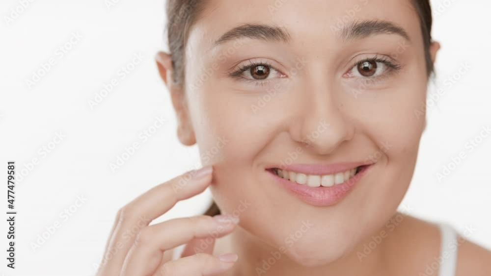 Horizontal close up of young gorgeous Caucasian brunette woman in white bra strokes her jaw line smiling wide for the camera on white background | Clean skin concept Horizontal close up of young gorgeous Caucasian brunette woman in white bra strokes her jaw line smiling wide for the camera on white background | Clean skin concept