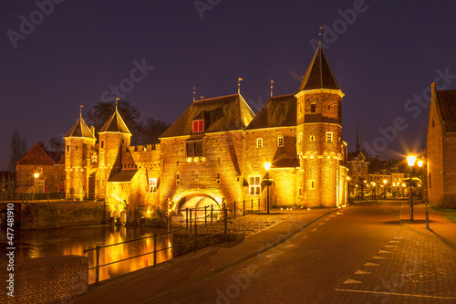 Illuminated historic land and water gate de Koppelpoort at night in Amersfoort.