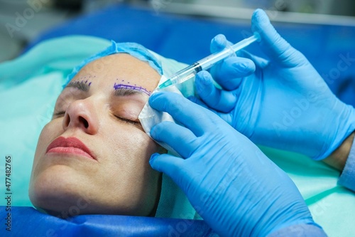 Plastic surgery for eyebrow correction. Woman patient is lying on the operating table, doctor gives her an injection for anesthesia before the operation