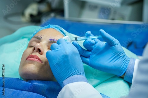 Plastic surgery for eyebrow correction. Woman patient is lying on the operating table, doctor gives her an injection for anesthesia before the operation