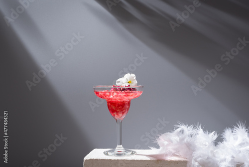 Glass of pomegranate margarita with flower blooms near near feathers photo