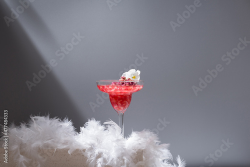 Glass of pomegranate margarita with flower blooms near near feathers photo