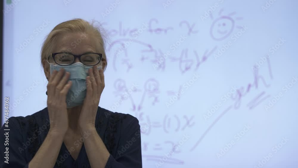 Portrait of mature woman teacher smiling and putting on face mask in front of an interactive whiteboard in a classroom. Portrait of mature woman teacher smiling and putting on face mask in front of an interactive whiteboard in a classroom.