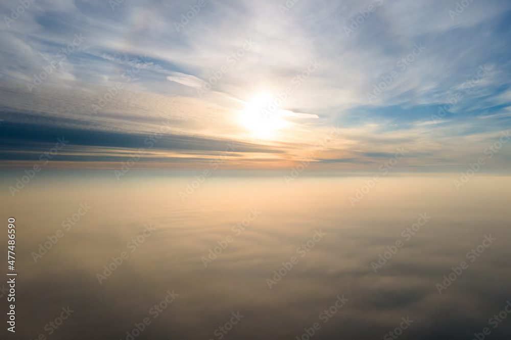 Aerial view of vibrant yellow sunrise over white dense clouds with blue sky overhead