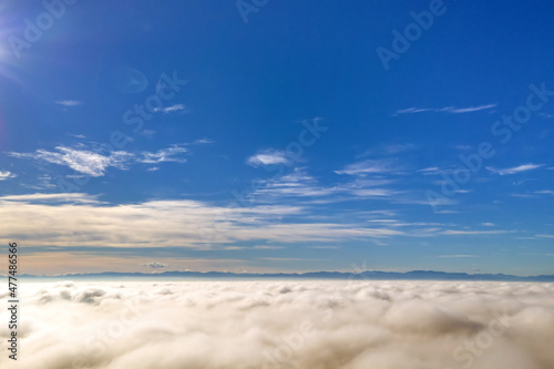 Aerial view of vibrant yellow sunrise over white dense clouds and distant mountains on horizon.