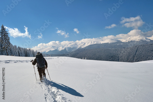 Man backpacker hiking snowy mountain hillside on cold winter day